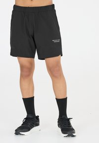 Svarta sportshorts med elastisk midja, sidofickor, broderad logotypdetalj och en slät textur, kombinerat med svarta sneakers.