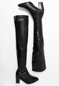 Bottes noires en faux cuir au-dessus du genou avec un talon haut chunky. Elles possèdent une fermeture éclair latérale et une texture lisse, avec un design ajusté.