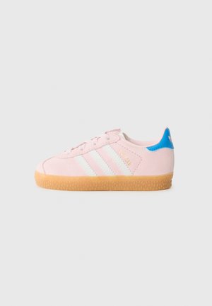 Sneaker en suède rose clair avec trois bandes blanches, semelle en caoutchouc beige et accent bleu au talon. Les lacets et le col rembourré complètent le design.
