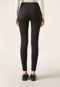 Jeans ajustados de tiro alto negro con una textura suave, dos bolsillos traseros y un diseño ceñido, combinados con zapatos planos negros.