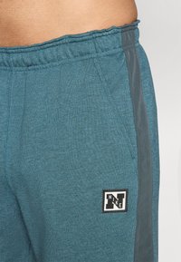 Tumbraijas bikses izgatavotas no mīksta auduma, ar elastīgu jostu, sānu paneļiem tumšākā tonī un melnu Nike logu.