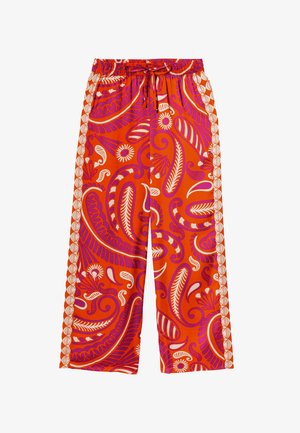 Pantalon large rouge avec un motif paisley et floral vibrant en rose et blanc. Présente une taille élastique et un cordon de serrage.