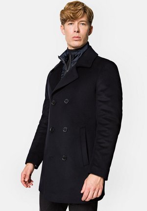 Granatowy wełniany płaszcz typu peacoat z podwójnym zapięciem, dużymi guzikami i wyłogi. Teksturowana tkanina i kieszenie boczne. Nałożony na pikowany jacket.