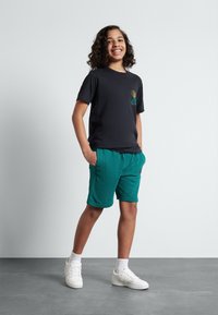 Svart kortermet T-skjorte med gull- og teal-grafikk; teal shorts med lommer; hvite sneakers; glatt tekstur; uformell passform.