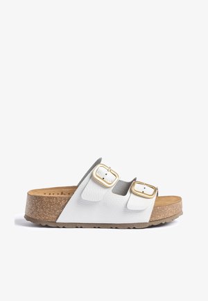 Witte sandaal met open teen, twee gouden gespen, kurken zool en een bruin voetbed, zijaanzicht tegen een witte achtergrond.