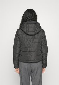 Svart puffjacka med huva, med horisontell sömnad och en slät, glänsande yta. Bärs med grå, strukturerade byxor.