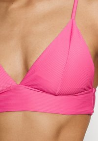 Top de biquíni rosa com textura canelada, design triangular, alças finas e ajustáveis, e uma faixa larga por baixo do busto. Textura suave e minimalismo nos detalhes.