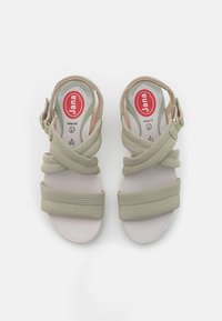 Beige sandals with cross straps made of textured fabric, cushioned insole, and adjustable buckle. Flat sole with a lightweight design.