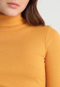 Rippierter, taillierter Rollkragenpullover in leuchtendem Orange. Verfügt über einen hohen Kragen und lange Ärmel, die eine weiche Strickstruktur zeigen.