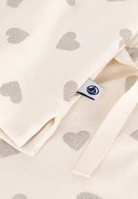 Tessuto di cotone in un beige crema con piccoli cuori argentati glitterati. Include un'etichetta cucita con un logo e nastri in tessuto coordinato.