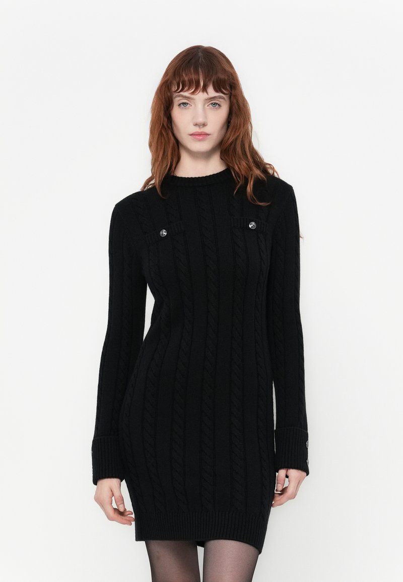 Abito nero lavorato a maglia con texture a coste, girocollo e maniche lunghe. Presenta bottoni decorativi sulle spalle e polsini a coste.