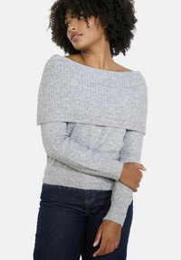 Gray off-the-shoulder sweater with a ribbed texture, long sleeves, and a soft fabric. Worn with dark denim jeans.
