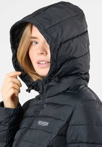 Zwarte pufferjack met een capuchon, ritsclosure en ingestikte verticale panelen. Bevat "SEASIDE" branding aan de voorkant. Glad, glanzend textuur.