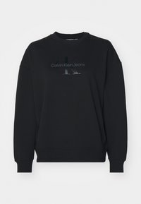 Svart hettegenser laget av mykt stoff, med rund hals, senkede skuldre og en glanset "Calvin Klein Jeans" logo på forsiden.