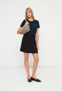 Camiseta navy con diseño de corazón, falda negra con bolsillos y detalle de botones, y un bolso de mano texturizado con estampado de serpiente. Zapatos planos marrones.