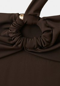 Tessuto marrone scuro attorcigliato e raccolto intorno a un anello di metallo dorato, formando un elegante dettaglio a nodo su un indumento.