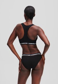 Il reggiseno sportivo nero e gli slip coordinati presentano un'ampia fascia con marchio. Il tessuto sembra liscio e elasticizzato con un design senza cuciture.