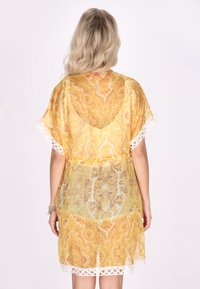 Kerge kollane kimono paisleimustriga, krošeedetailidega varrukatel ja avatud seljaga disain, millel on keerukad tekstuurid ja kerge kangas.