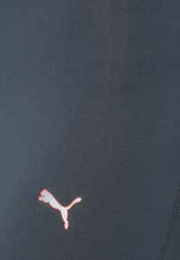 Leggings de sport gris foncé à texture côtelée, avec un petit logo Puma rouge sur le côté gauche. Conçus pour le confort et la mobilité.