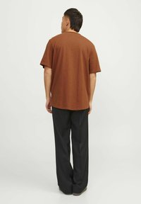 Smeđi kratki rukavi T-shirt s opuštenim krojem, izrađen od teksturirane tkanine, uparen s crnim širokim hlačama. Vidljivi šavovi na rubu.