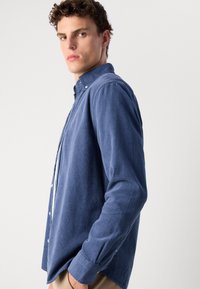Blauwe button-up shirt van corduroy stof, met een klassieke kraag, lange mouwen en een ontspannen pasvorm. Getextureerd oppervlak met subtiele ribbels.