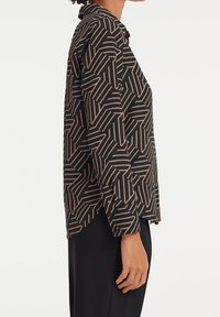 Chemise noire avec un motif géométrique doré, col à revers, manches longues et coupe droite, avec des détails à boutons aux poignets.