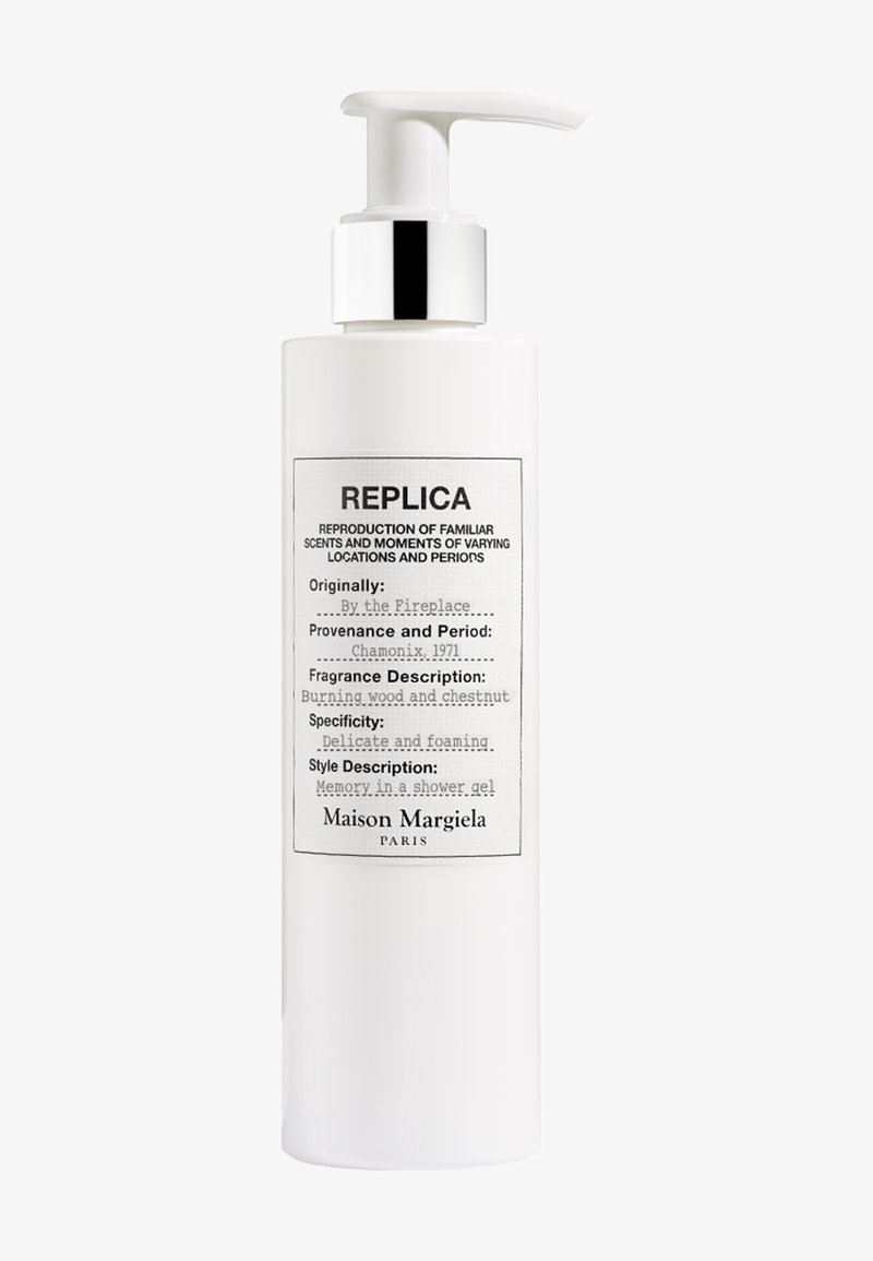 Hvit pumpeflaske med Maison Margiela Replica dusjgelé, merket "By the Fireplace", duftnoter inkluderer brennende ved og kastanje.