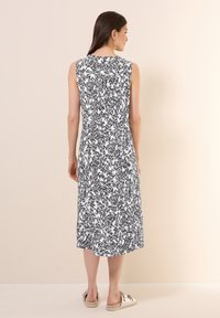 Ärmelloses Midikleid in einem schwarz-weißen abstrakten Muster, mit rundem Halsausschnitt und geradem Saum. Tragen mit lässigen Slippern.