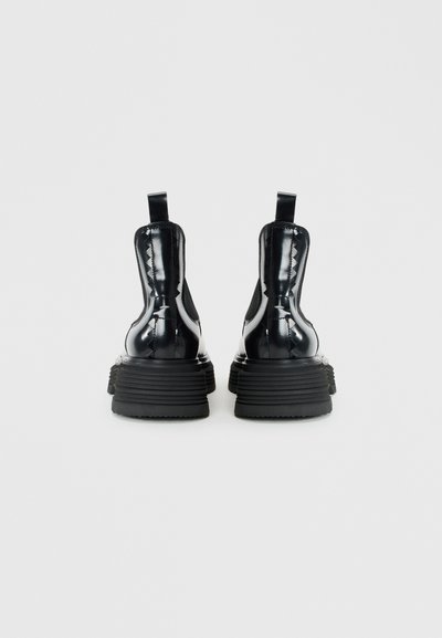 Bottines en cuir verni noir avec des semelles en caoutchouc crantées, des panneaux latéraux élastiques et des sangles à l'arrière pour un enfilage facile. Accents texturés sur les côtés.