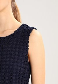 Námořnický bezrukávový top s texturovanou, vzorovanou tkaninou s vyvýšenými diamantovými tvary a vlnitými okraji na ramenou.