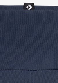 Tissu bleu marine avec une texture côtelée, présentant une étiquette noire avec un design d'étoile blanche et de flèche en haut. Design minimaliste et élégant.