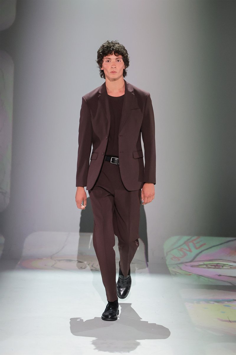 Donkerburgundy pak met een getailleerde blazer en taps toelopende broeken, gecombineerd met een zwart shirt met ronde hals en gepolijste zwarte schoenen op de catwalk.