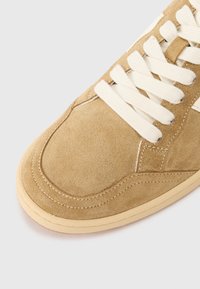 Beige nubuk bőr sportcipő fehér fűzökkel, kerek orral, kontrasztos varrással és minimalista dizájnnal.