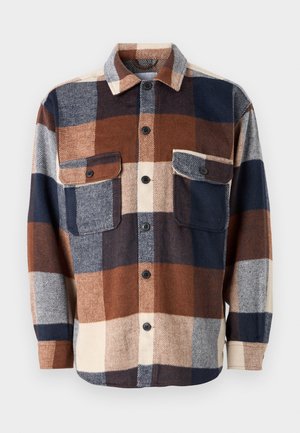Chemise en flanelle à carreaux marron, bleu marine et crème. Présente un devant à boutons, deux poches poitrine et un col évasé. Texture douce.
