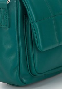 Borsa a mano in pelle verde acqua con design trapuntato, dotata di chiusura a patta e cuciture in evidenza. Texture liscia con tasche visibili e accenti metallici.