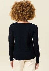 Marinsvett med långa ärmar och texturerade nätinsatser, rundad halsringning och en åtsittande siluett, tillverkad av mjukt stickat material.