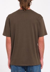 Bruine cotton T-shirt met korte mouwen en een ronde hals. De achterkant is eenvoudig met een rechte zoom, gecombineerd met blauwe denim jeans.