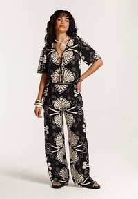 Fekete és krémszínű, összeillő öltözék, mely rövid ujjú, rövid fazonú, gombos ingből és kagyló- és virágmintás, bő szárú nadrágból áll.