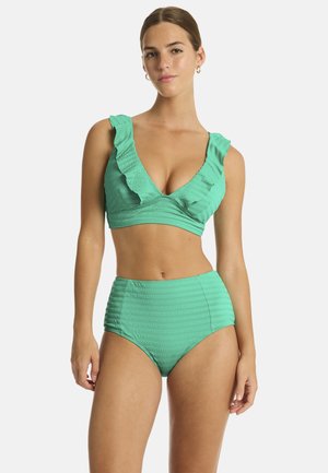 Kobieta ubrana w zielony, teksturowany dwuczęściowy strój kąpielowy z marszczonymi ramiączkami i wysokim stanem, stojąca na jednolitym tle.