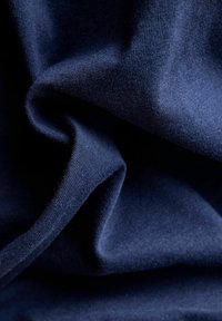 Granatowy materiał o gładkiej fakturze, z miękkim, elastycznym splotem i widocznymi cienkimi włóknami, złożony w sposób ukazujący głębię i cień.