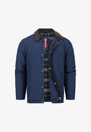 Quiltad marinblå jacka med krage i brunt manchester, tryckknapp och dragkedjestängning samt rutigt foder. Har diamantformad stickning och slitstarkt tyg.