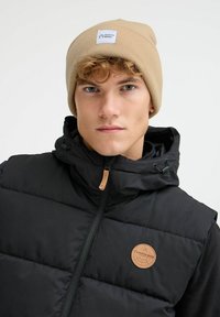 Svart puffervest med glidelås foran, hette og brun lærlogo. Beige strikket lue med et hvitt merke som sier "NORTH BEND."