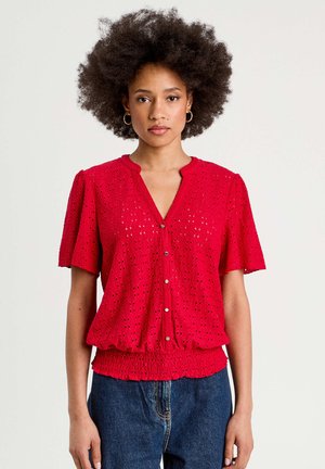 Blusa corta rossa a maniche corte con un motivo testurizzato, dotata di abbottonatura frontale e una vita elastica per una vestibilità relax.