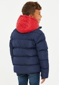Mørkeblå pufferjakke med en lys rød hætte, med kviltet design og elastiske manchetter. Varm, let og slidstærkt materiale.