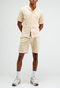 Beige shirt met korte mouwen en bijpassende shorts gemaakt van een textiel met structuur, voorzien van een ingesprongen kraag, knopen en zijzakken.
