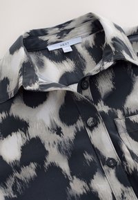 Collared button-up shirt with black, white, and gray abstract spotted pattern and visible brand label "NEXT" inside the collar.