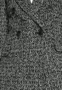 Dubbelgeknoopt jasje van textuurrijk zwart-wit stof. Voorzien van zwarte knopen en een getailleerde pasvorm met twee zijzakken.
