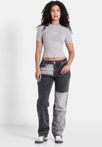 Top fitted a maniche corte grigio chiaro e pantaloni in denim neri con un pannello grigio chiaro in contrasto. Il modello indossa sneakers bianche con strisce nere.