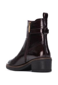 Botas de tobillo burdeos oscuras con una textura brillante, cremallera lateral y un tacón negro bajo. Presentan un detalle de línea cosida a lo largo de los lados.