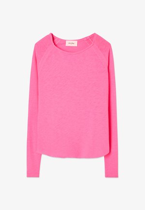 Dolga majica v svetlo rožnati barvi, narejena iz mehke tkanine. Ima sproščen izrez in zaobljen rob s šivanim okrasjem na rokavih.